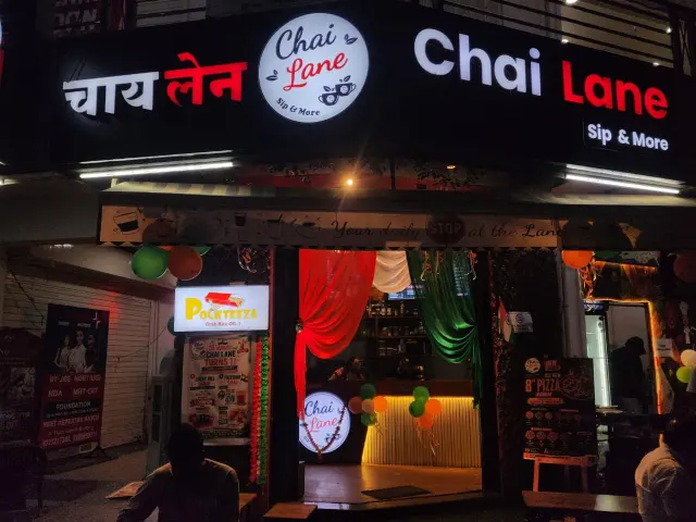 Chai Lane shopfront at night with its lit sign in Hindi and English, decorated with tricolour balloons and drapes.